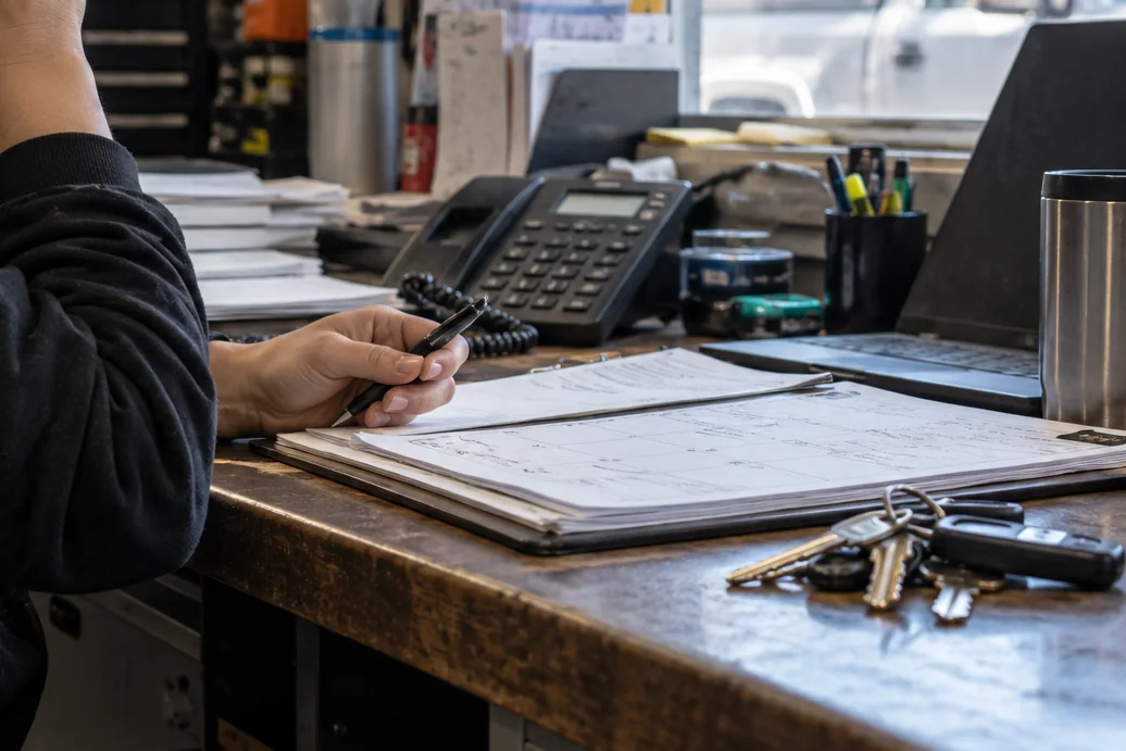 A small service-business workroom with a phone, paper schedule, and job keys
